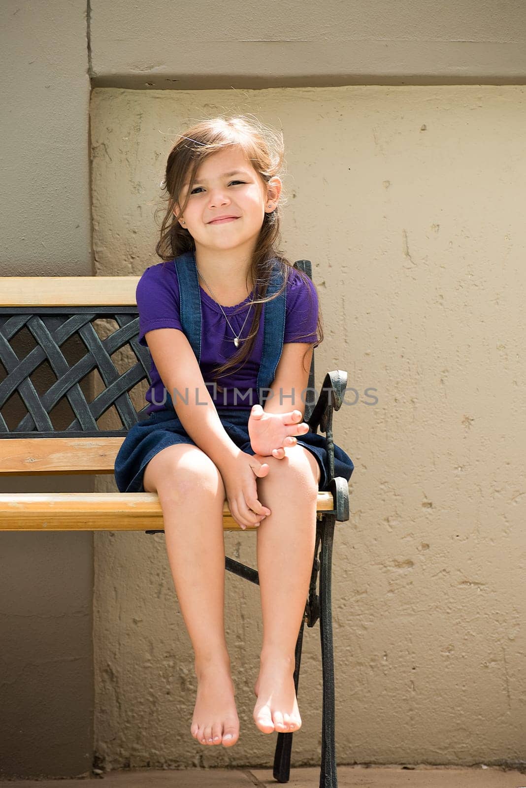 A little girl sits on a bench outside in the back garden of her home.
