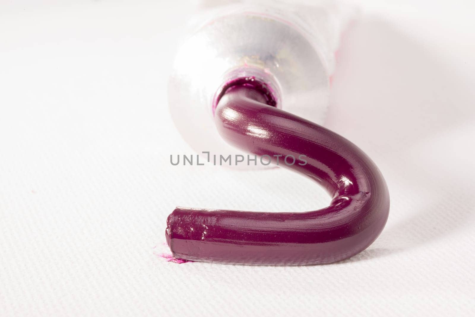 Magenta paste for oil painting is squeezed out of a tube on to a white canvas.