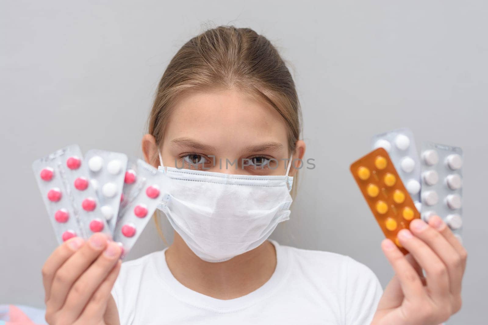 A girl with a medical mask on her face holds blisters with medicines