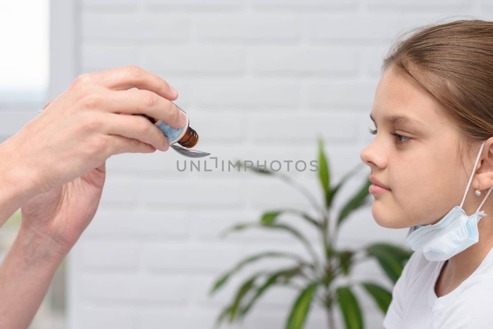 The doctor in the hospital pours medicine for a sick girl in a spoon