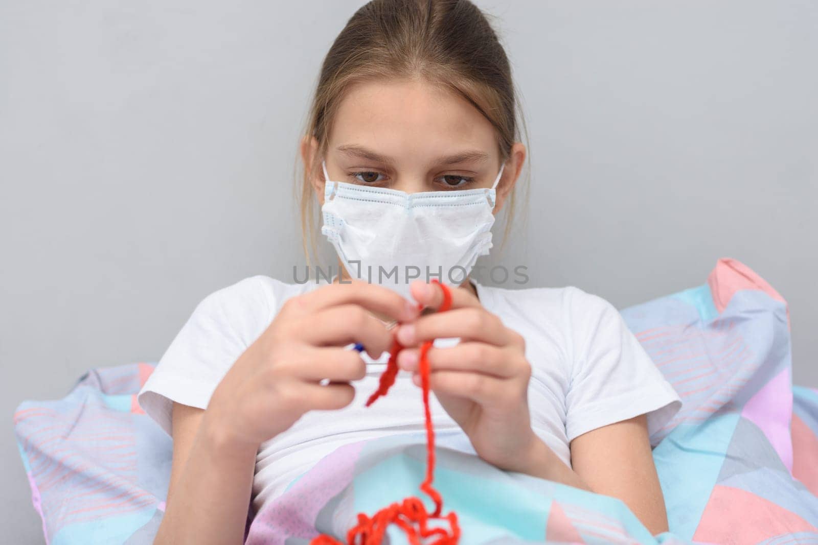 Ill girl in a medical mask knits lying in bed