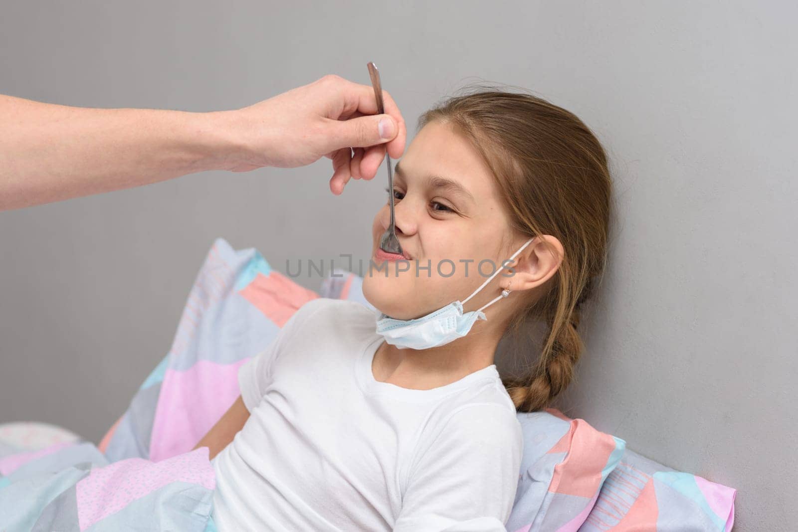 A sick girl is given medicine from a spoon in her mouth