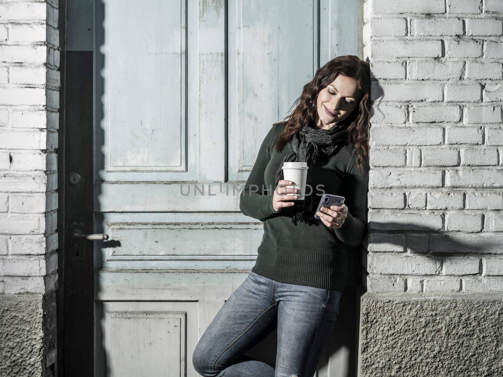 Young woman with red hair using her cellphone and drinking coffee from a takeout cup.