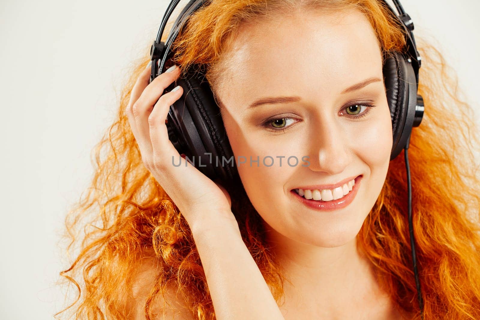 Photo of a beautiful young redhead listening to headphones and smiling.