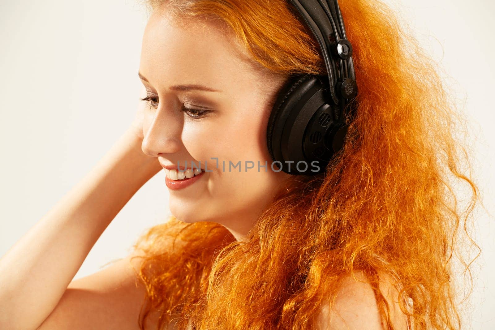 Photo of a beautiful young redhead listening to headphones and smiling.