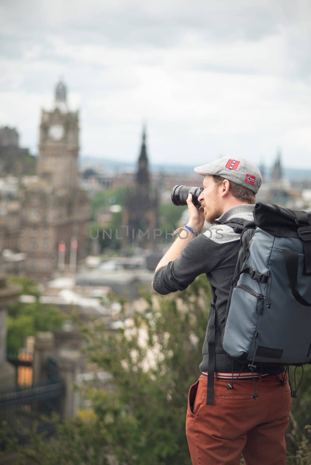 Photographer with backpack and a hat shooting buildings of Edinburgh in a sunny day