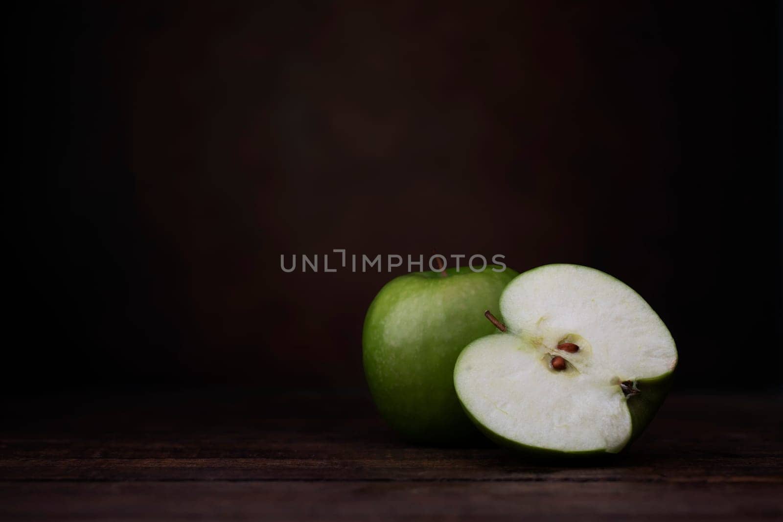 Two granny smith apples, one whole and one cut in half.  Two granny smith apples with old pottery jug.  Shot at eye level with dark rustic feel and copy space/