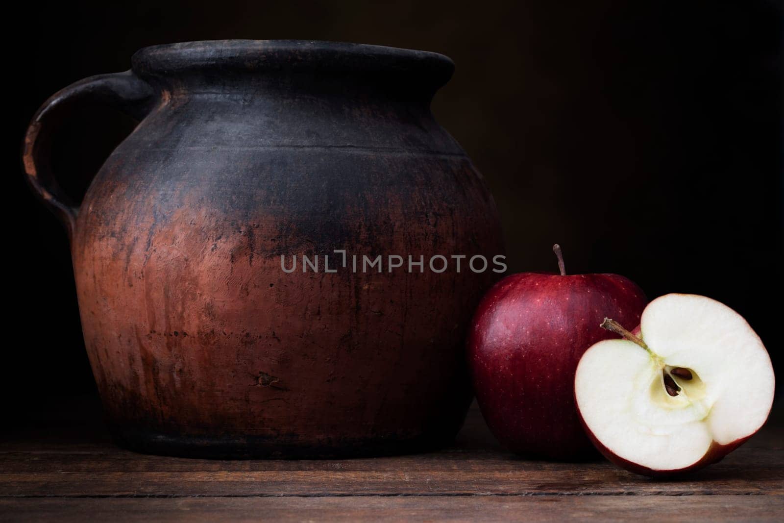 Two red apples, one whole one cut, with old pottery jug.  Shot at eye level with dark rustic feel.