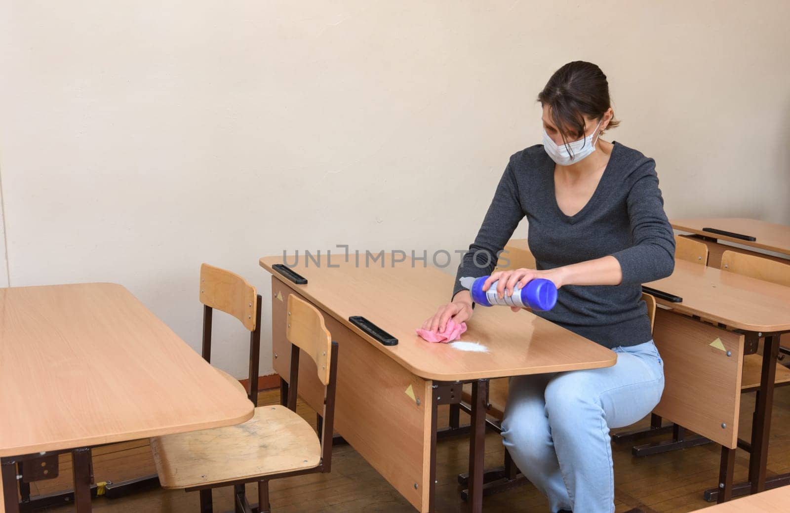 The girl pours cleaning and disinfectant on the desk at the school during the quarantine period