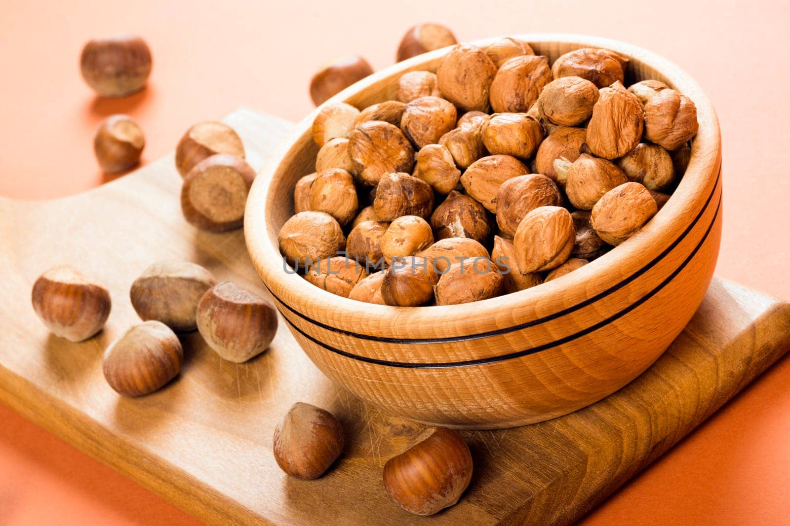 Fresh whole hazelnut fruit is in wooden dish on cutting board.