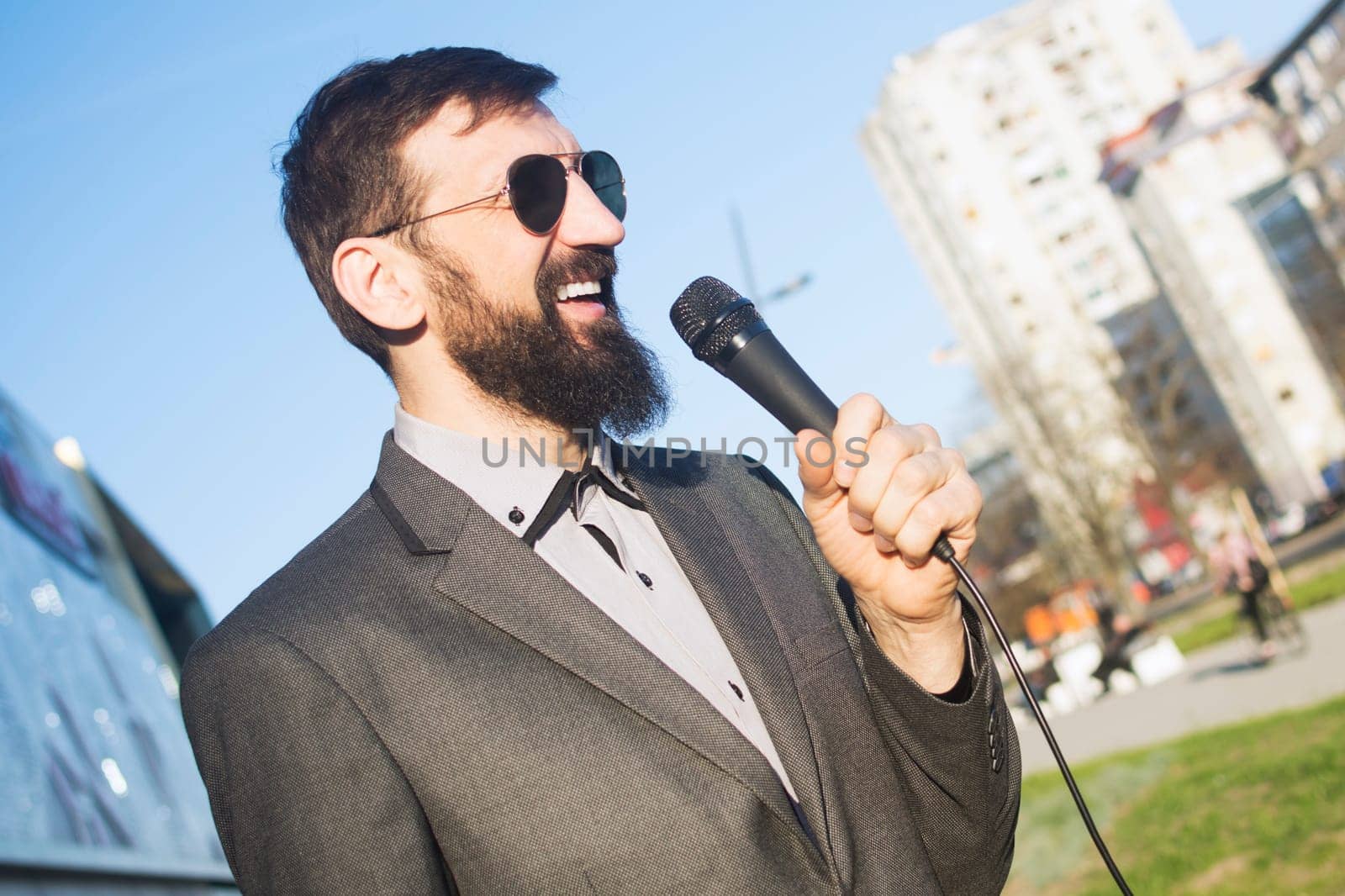 The smiling TV reporter or newscaster is speaking in microphone at the street in live program.