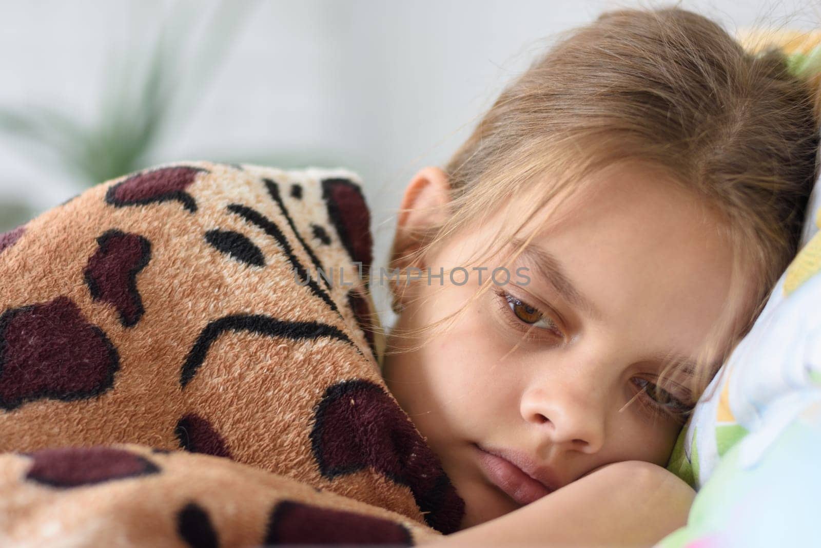 Girl slowly wakes up, lying in bed and covered with an old blanket