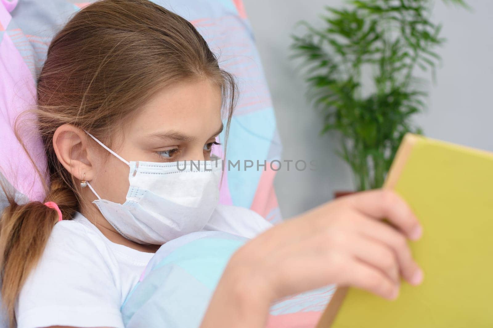 Girl reading a book while lying in bed in a hospital ward