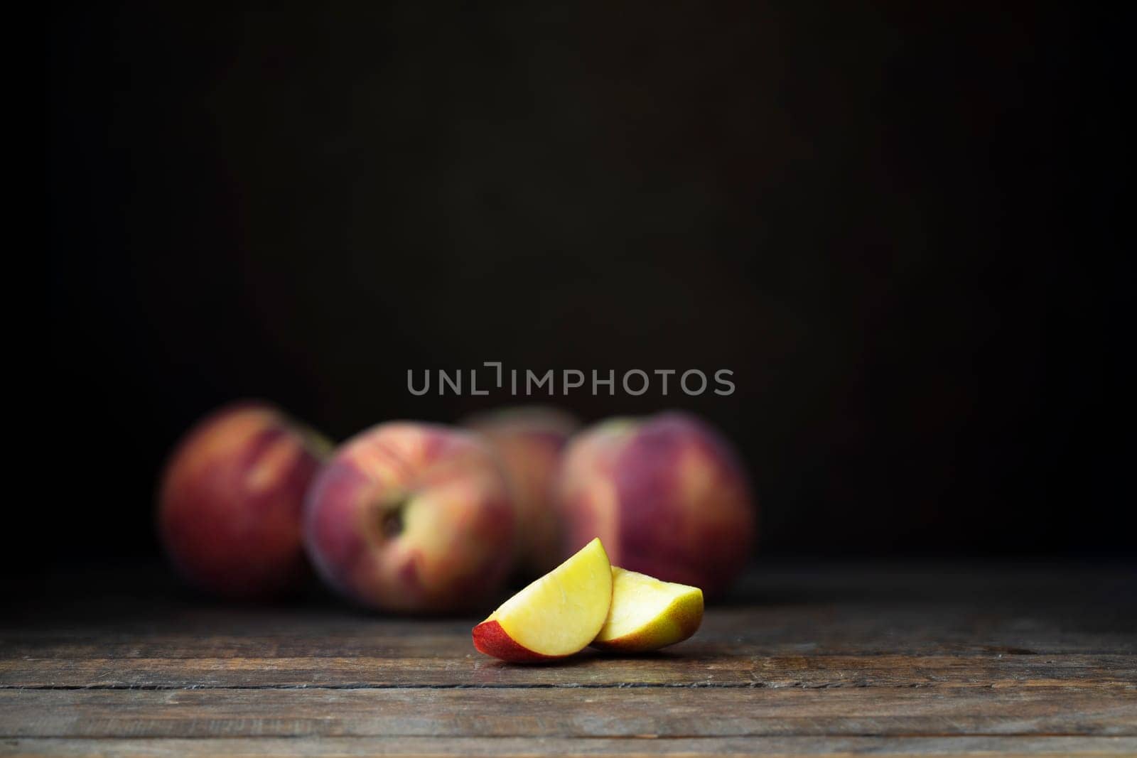 Fresh nectarines, whole and sliced, on  a rustic wooden table with a dark background