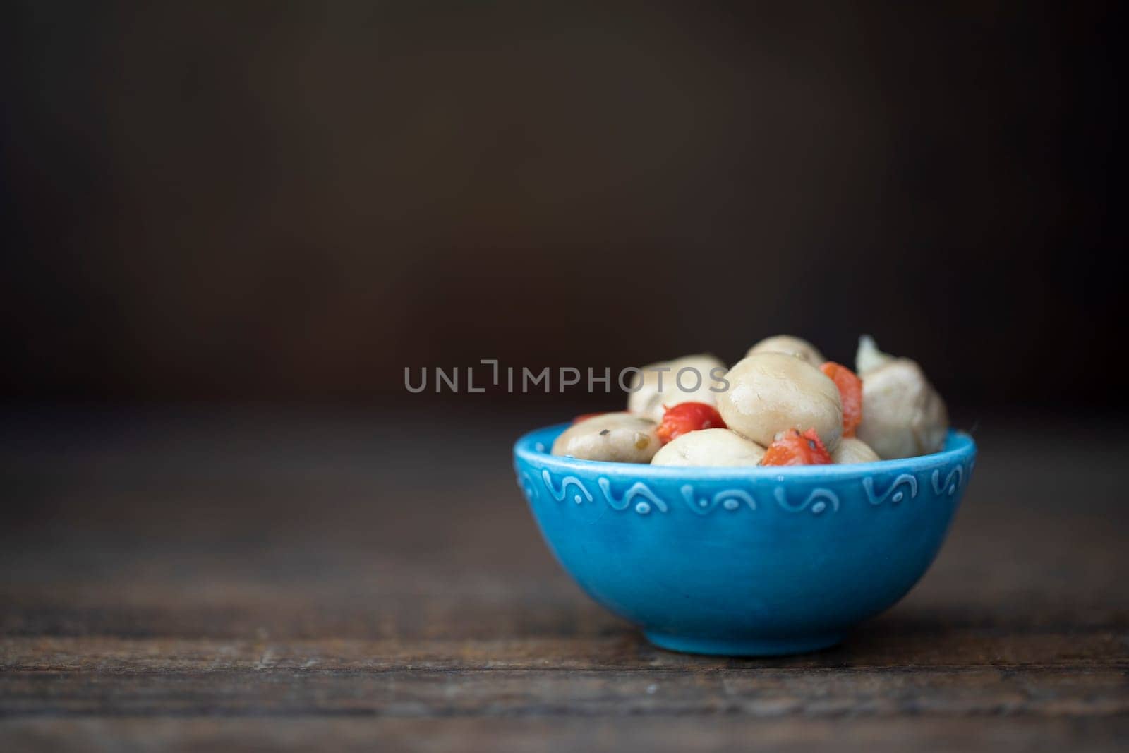 Marinated mushrooms tapas in greek ceramic bowl on wooden tablewith copy space.