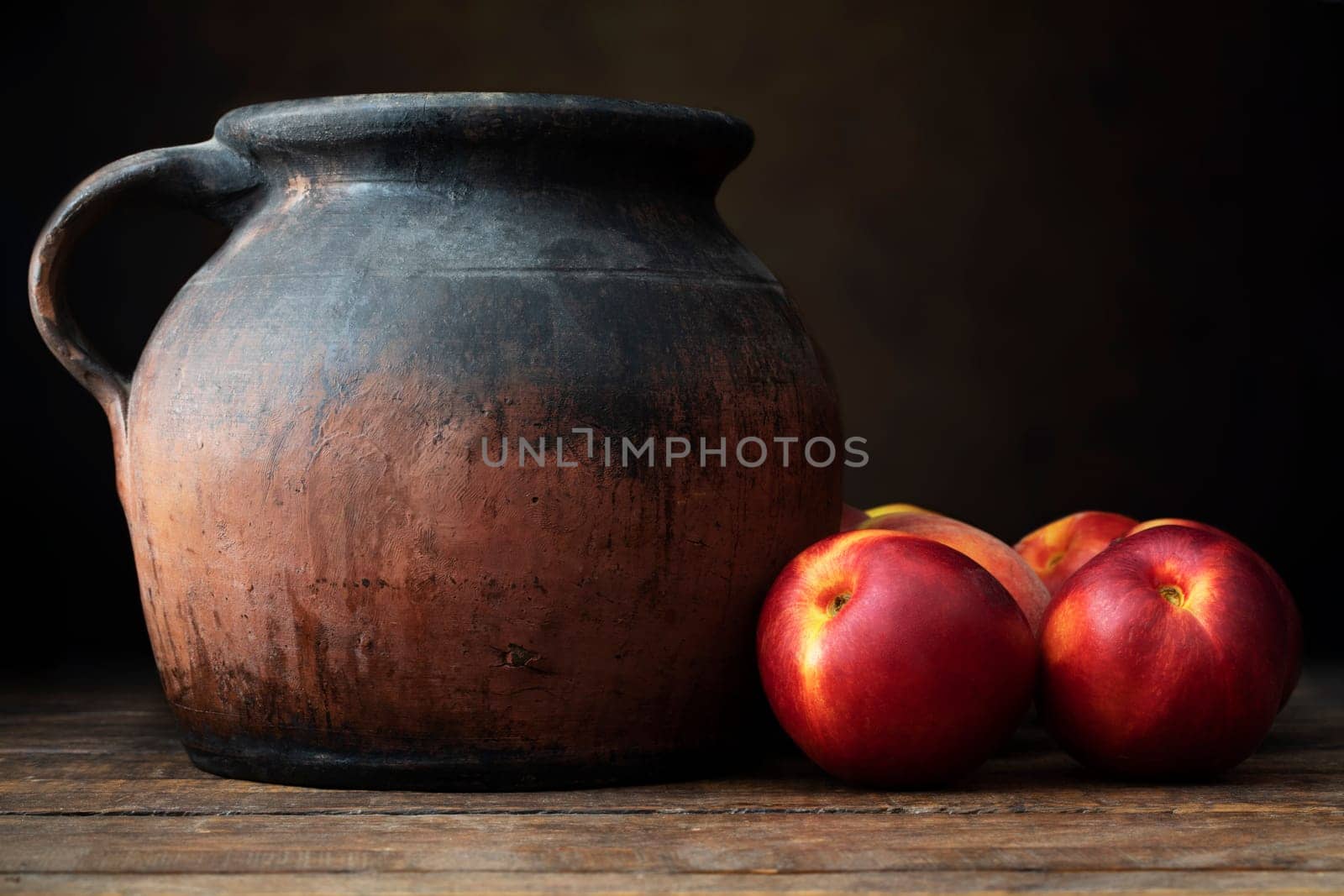Fresh nectarines next to a rustic pottery jug, on  a wooden table with a dark background