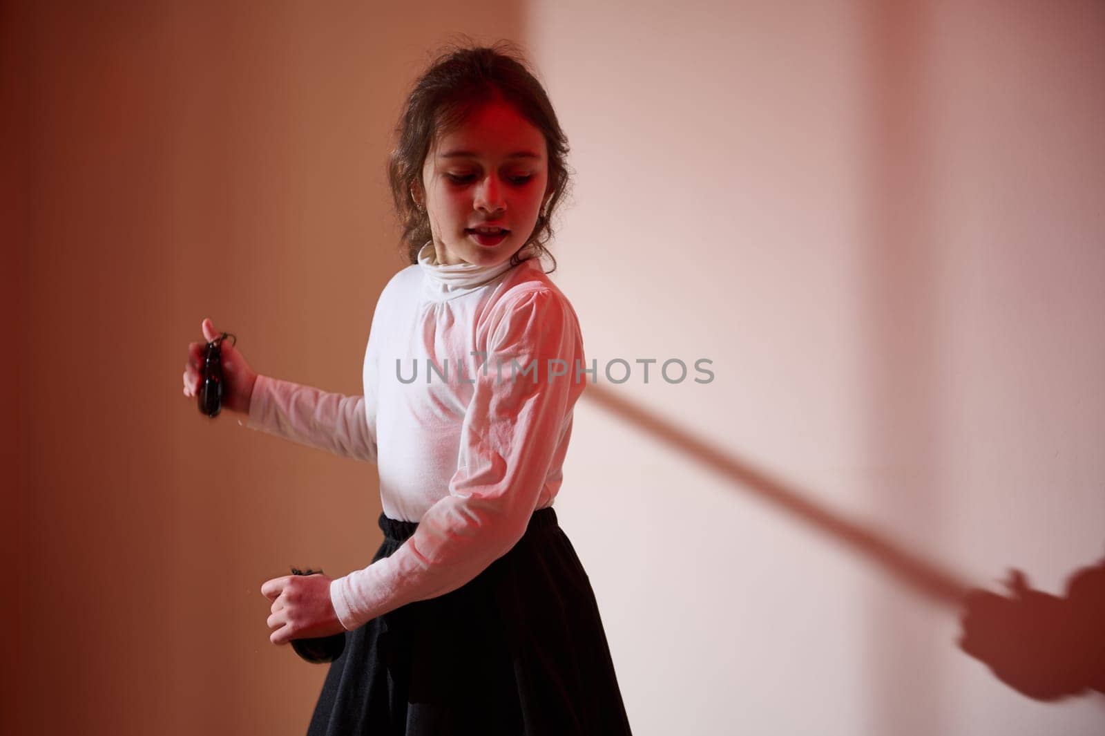 A young girl performs a dance move illuminated by warm colored lighting, creating a contrast between shadow and light, emphasizing expressive motion and emotion.