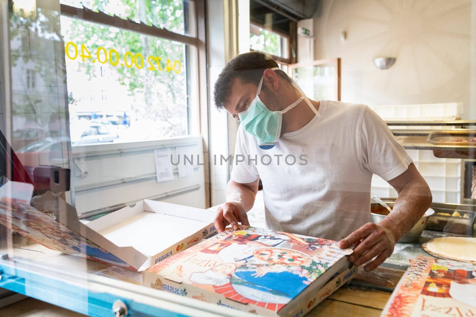 Man is working in a pizza restaurant drive with his mask and covid 19 protection. Pandemic situation