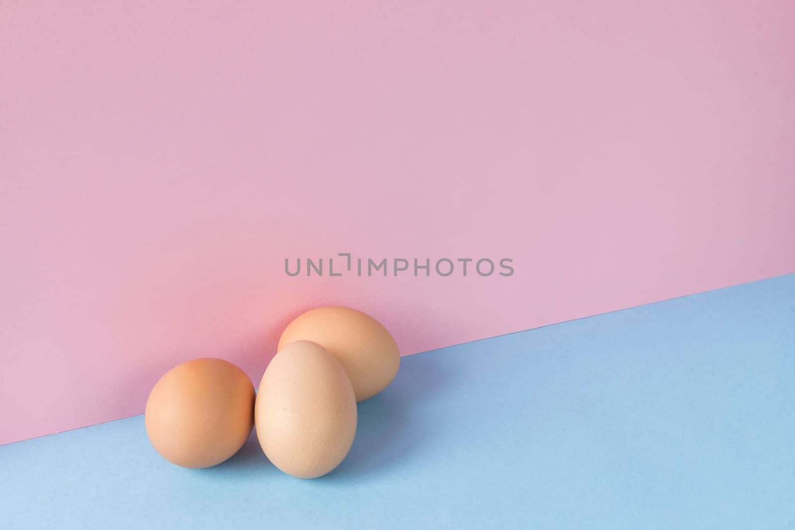 Minimalist image of three brown eggs on a light blue and pink background. Copy space available.