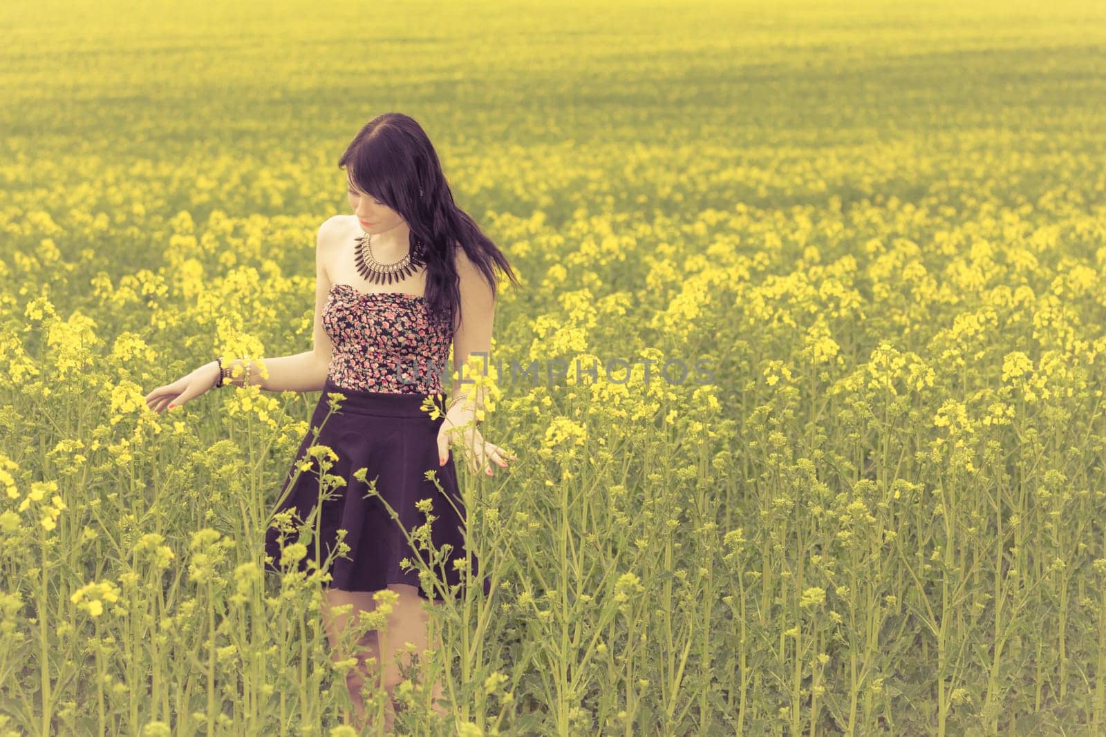 Attractive young beauty girl enjoying the warm sunny sun in nature rapeseed field takes time feeling sustainability and contemplation.
