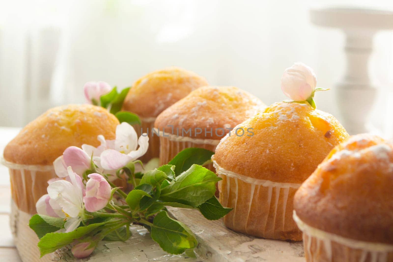 Golden muffins with powdered sugar and spring flowers Tasty dessert with sunny light.