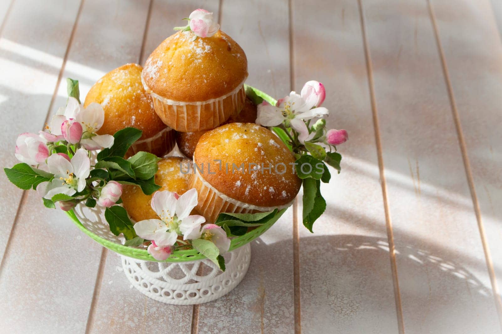 Small freshly muffins in lace wicher basquet and spring flowers on shabby table, copy space
