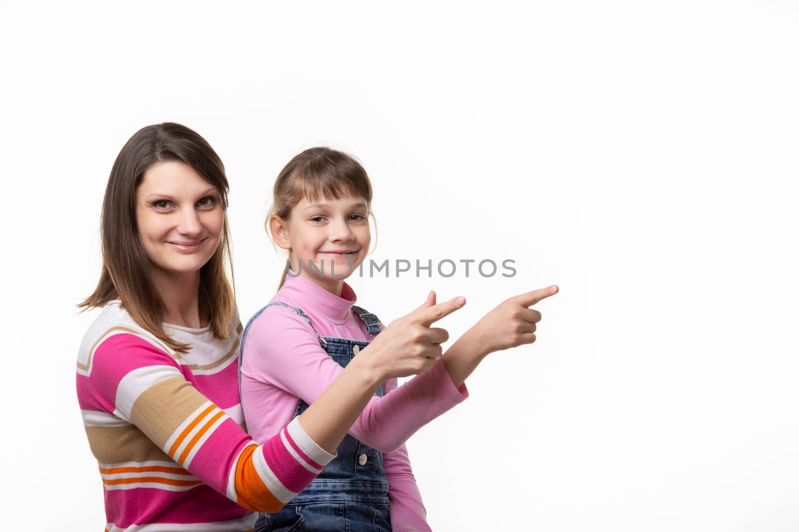 A girl sits on her mothers lap and joyfully points a finger at an empty place, looks into the frame