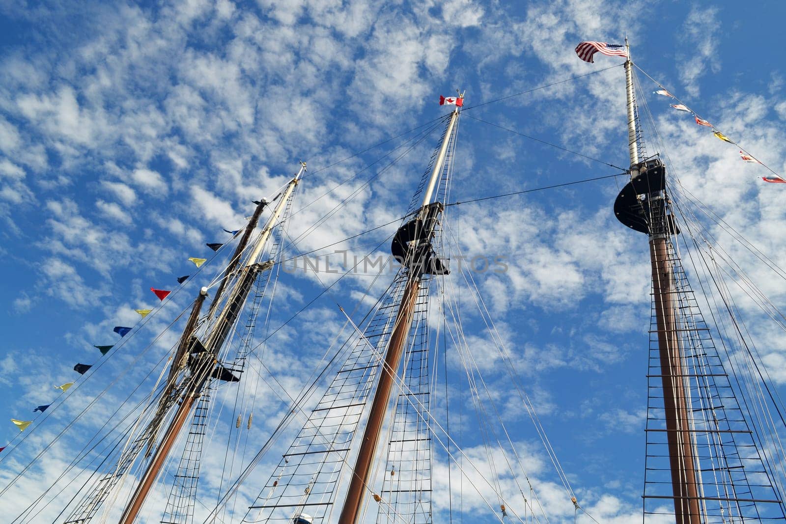 The tree masts of a large tall ship with there flags under a sonny sky.with some white clouds.