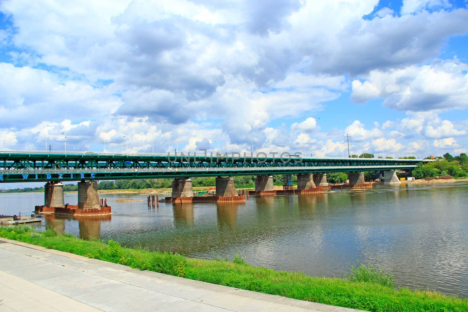 Long bridge over Wisla in Warsaw. Modern bridge over Wisla River in Warsaw. Landscape with river clouds and bridge in city. Embankment along banks of Wisla River and bridge