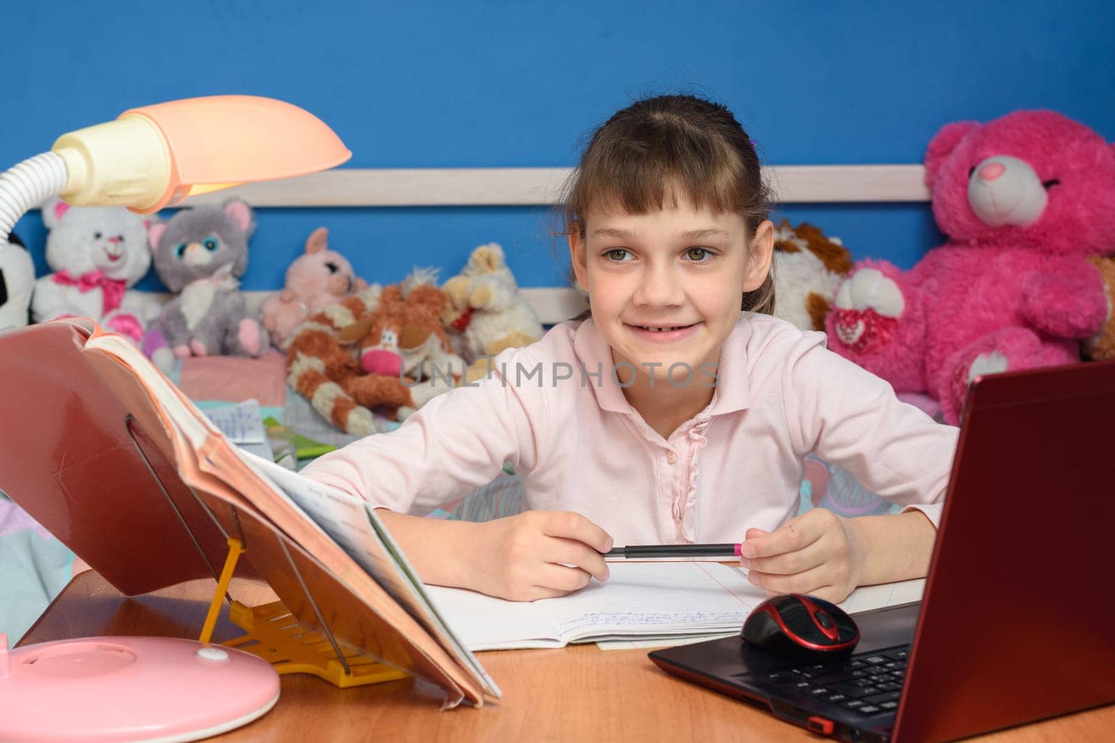 The girl in the children's room sits at the desk with a smile and does her homework