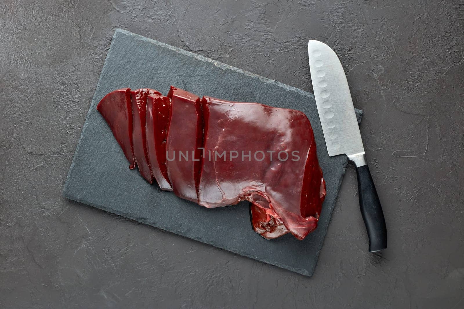 Raw beef livers on a black stone cutting board  on dark background. Top view