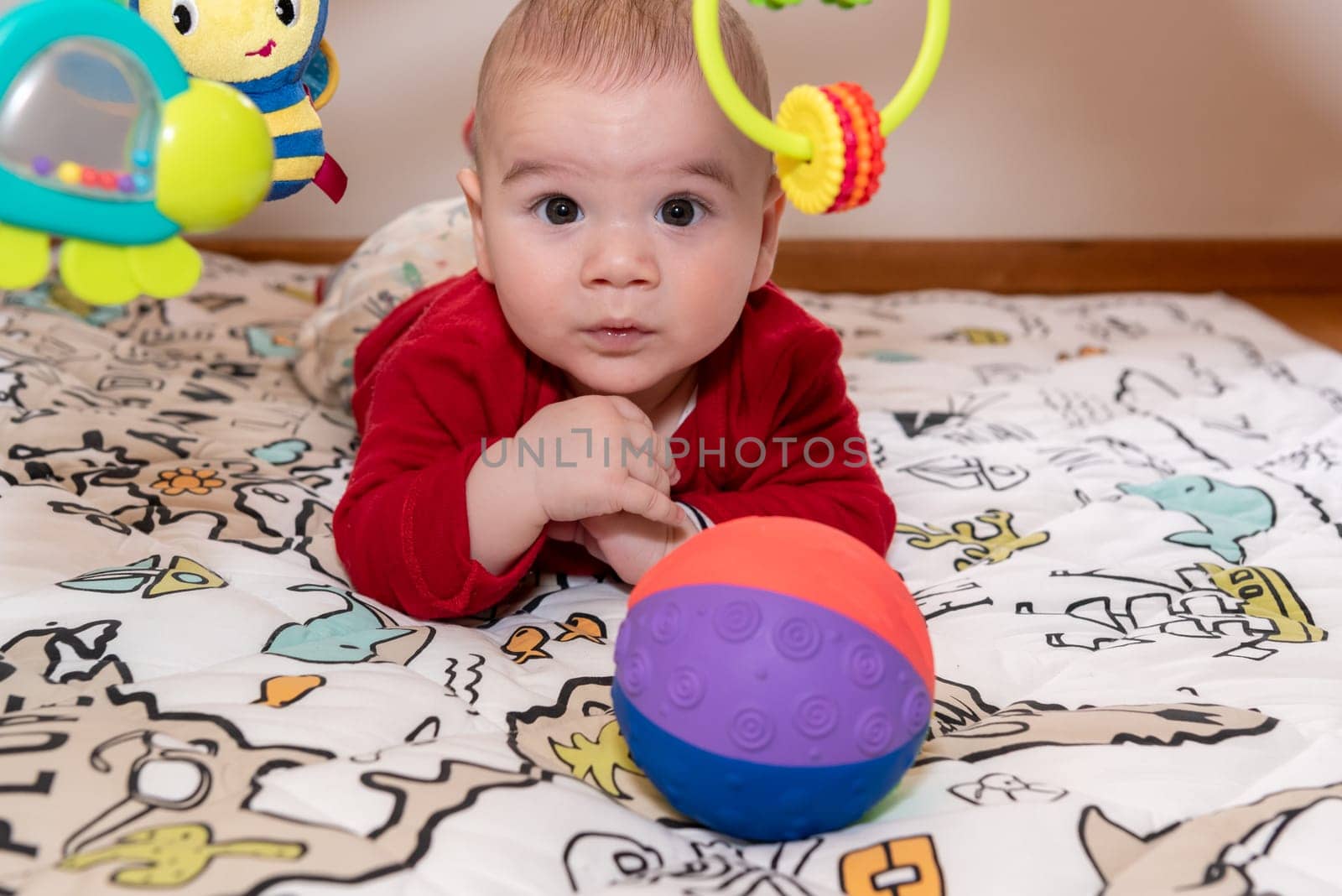 Adorable 6 months old little baby boy during tummy time surrounded by colourful toys