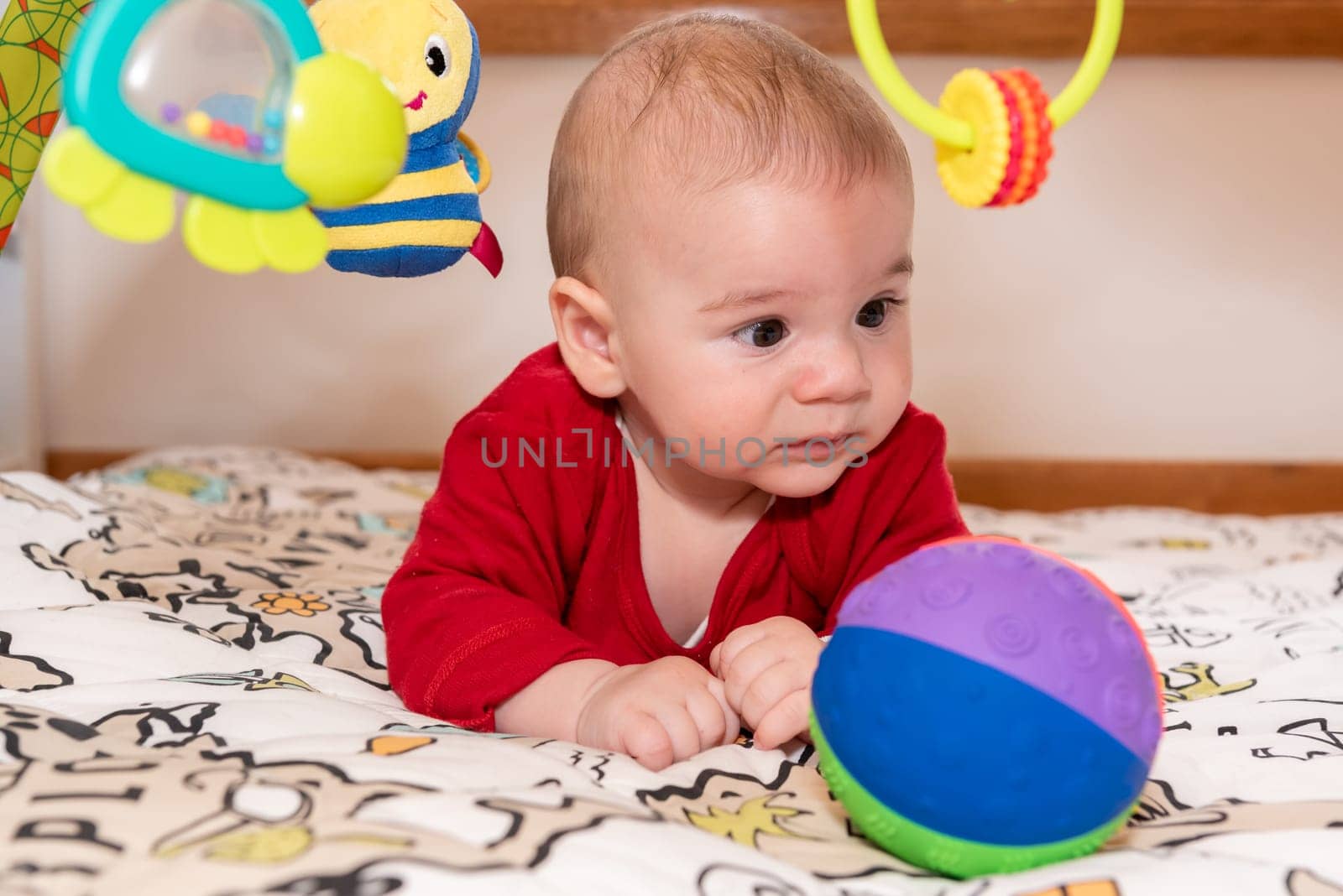 Adorable 6 months old little baby boy during tummy time surrounded by colourful toys