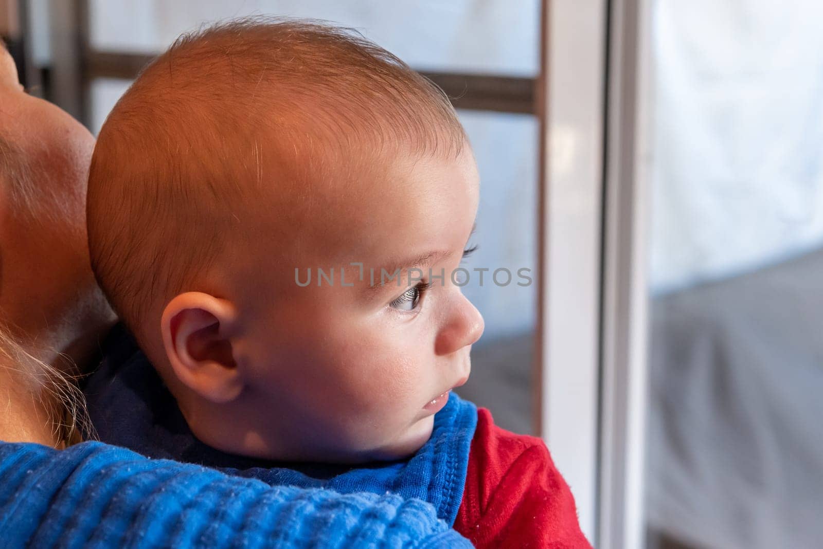Cute 6 months little baby boy with curiosity expression on his face in his mothers arms