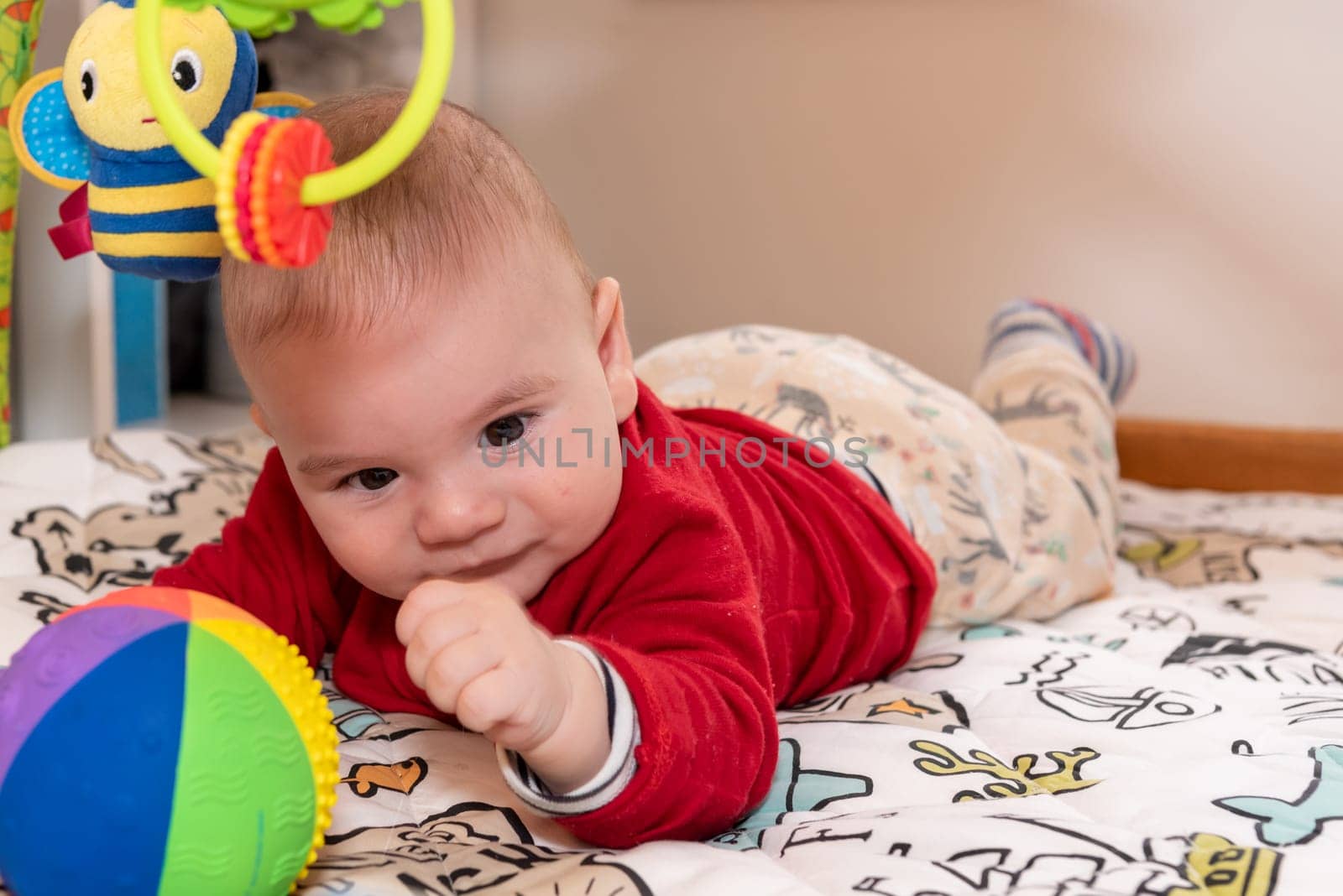 Adorable 6 months old little baby boy during tummy time surrounded by colourful toys