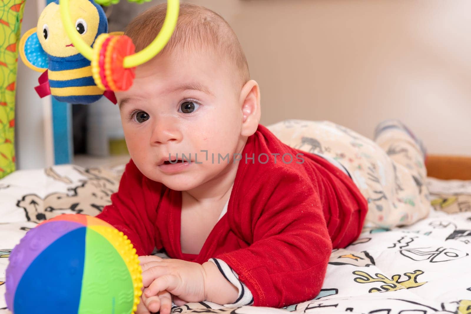 Adorable 6 months old little baby boy during tummy time surrounded by colourful toys