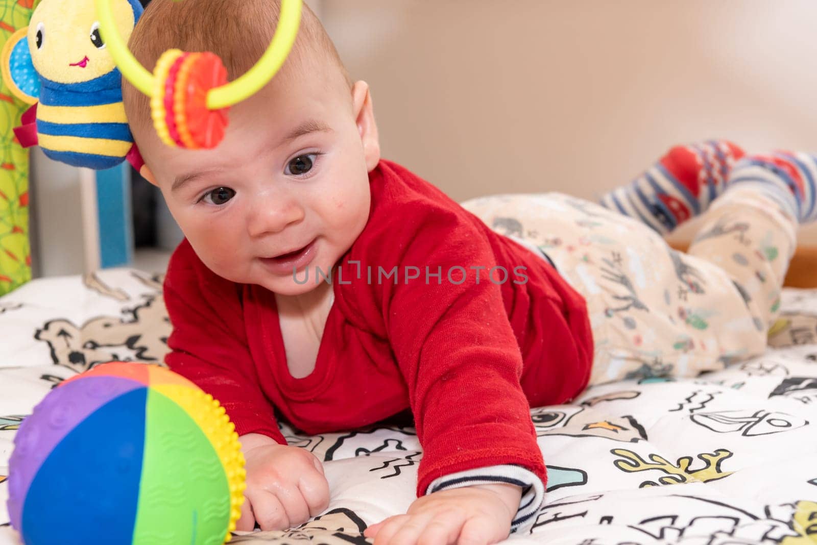 Adorable 6 months old little baby boy during tummy time surrounded by colourful toys