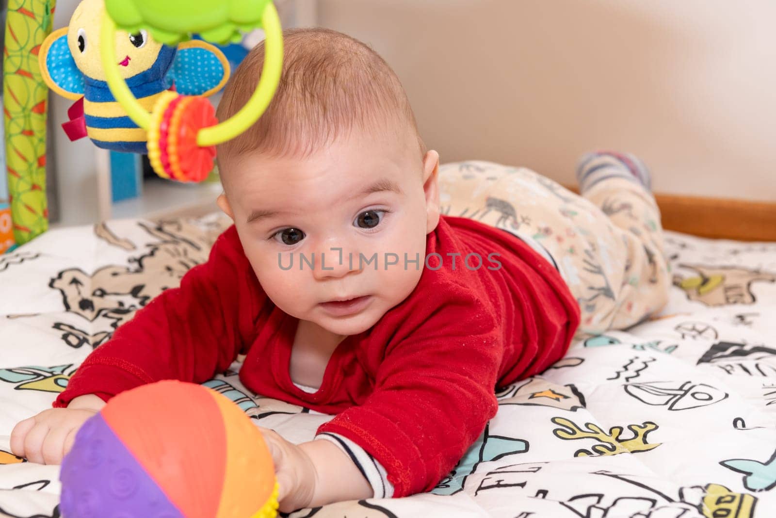 Adorable 6 months old little baby boy during tummy time surrounded by colourful toys