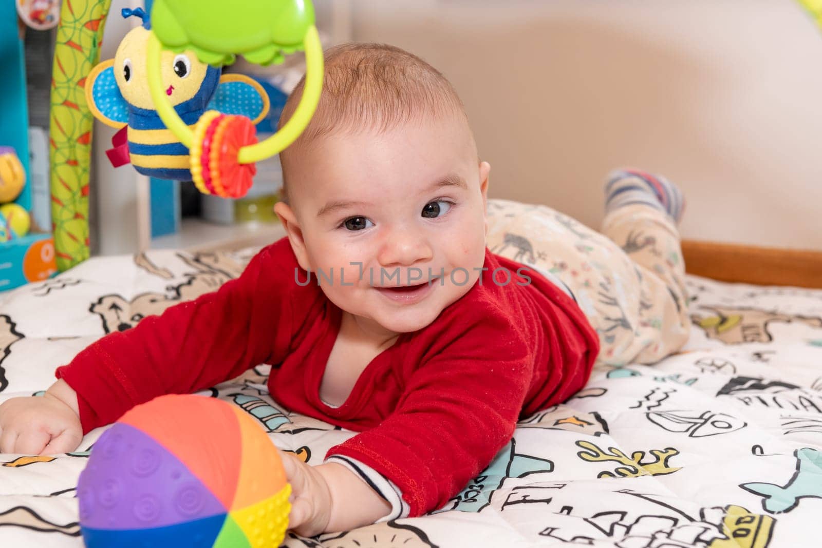 Adorable 6 months old little baby boy during tummy time surrounded by colourful toys