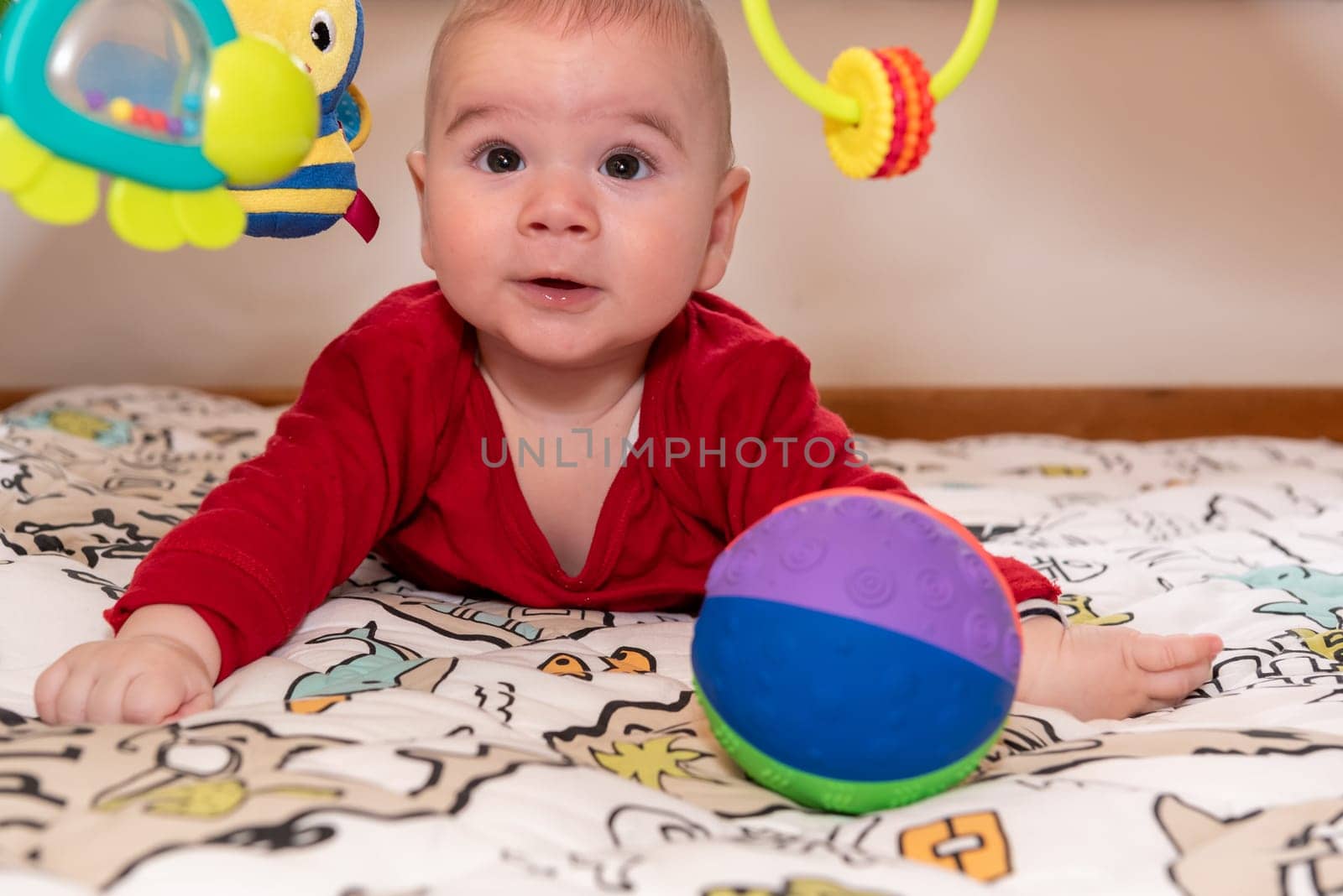 Adorable 6 months old little baby boy during tummy time surrounded by colourful toys