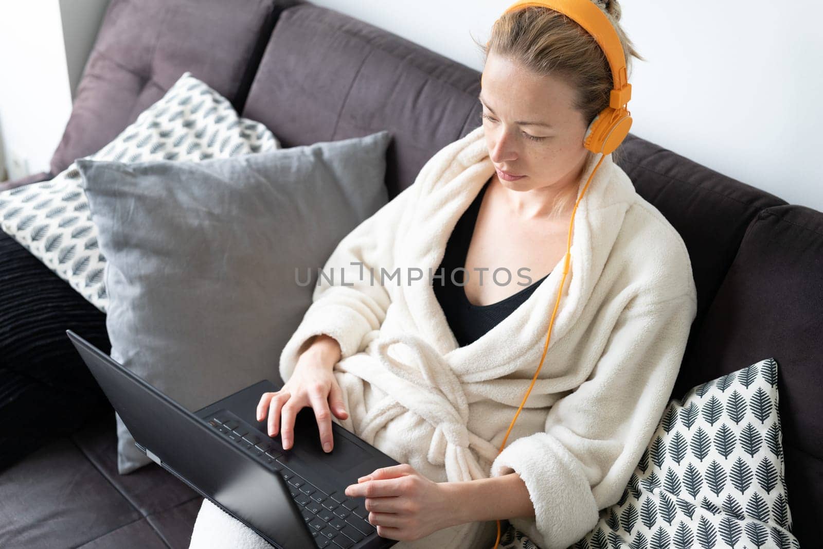 Stay at home, shelter in place and social distancing. Woman in her casual home bathrobe relaxing while working remotly from her living room. Using social media apps for video chatting.