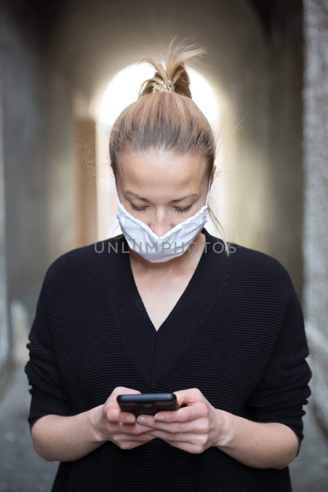COVID-19 pandemic coronavirus. Casual caucasian woman at medieval city street using mobile phone, wearing protective face mask against spreading of coronavirus and disease transmission.