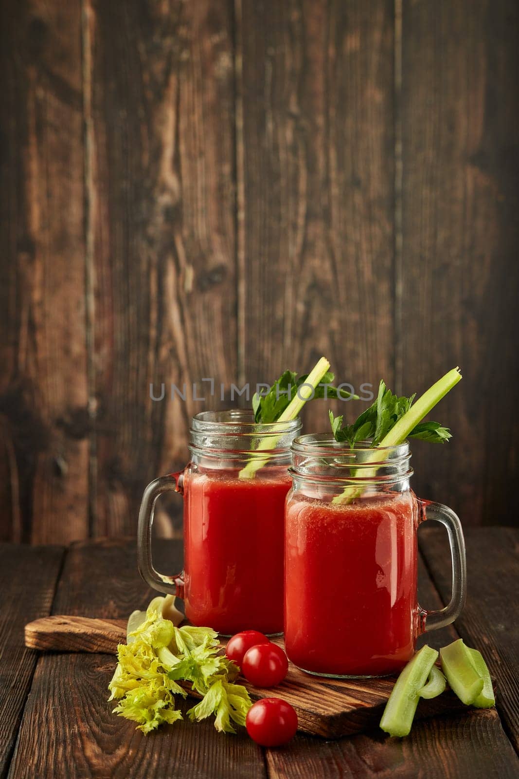 Two glasses with fresh tomato juice, celery, parsley and ripe tomatoes on dark brown wooden background. Healthy beverage, vegetable juice