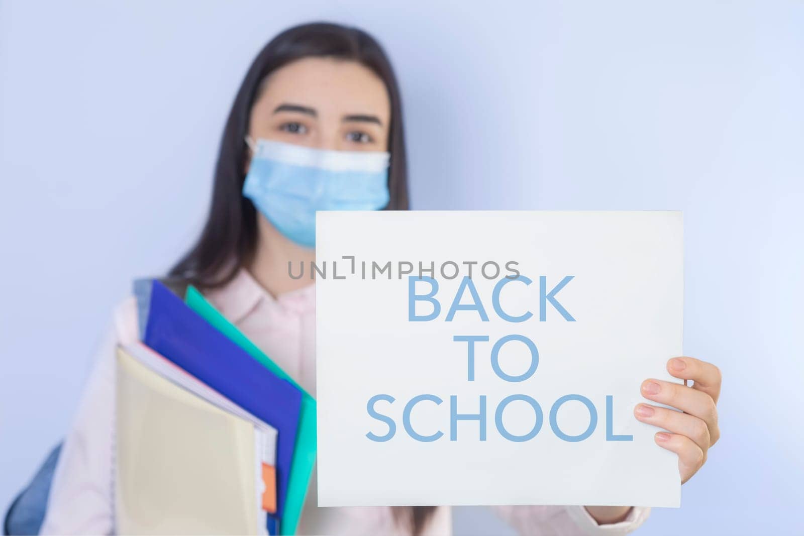 High school girl with mask on her showing back to school message. Student girl ready for school during the coronavirus pandemic. Focus on her hand with paper.