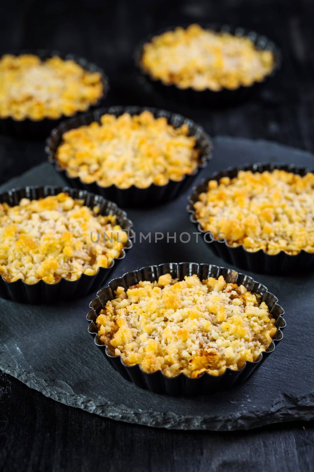 Small and delicious apple pies or apple crumble on black background. Apple tart.