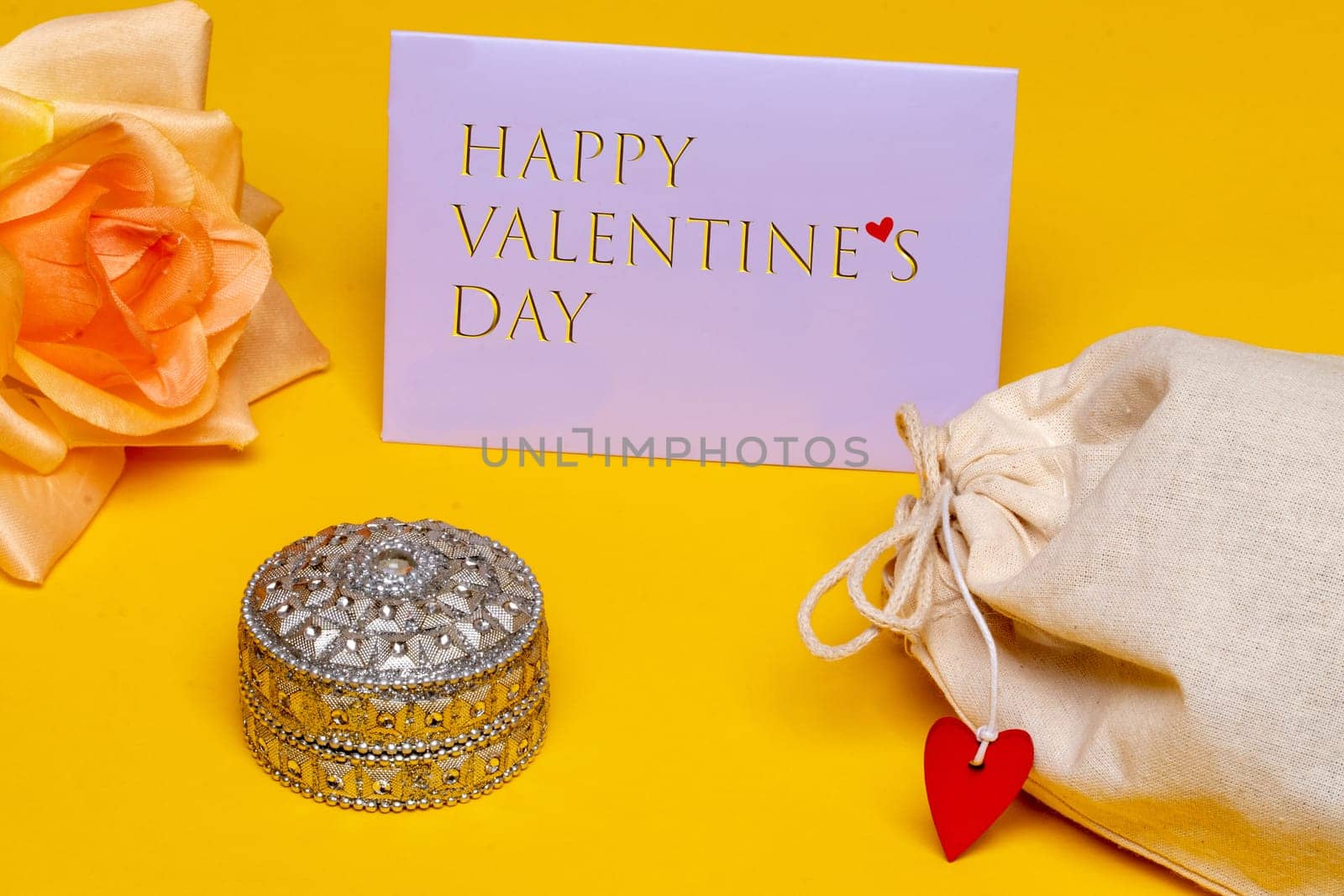 Valentines day greeting card. Close-up of a Jewellery box and beautiful yellow blossom of flower and a tag with inscription Happy mothers day and fabric gift drawstring bag on yellow background. Beauty for the mom. Macro.