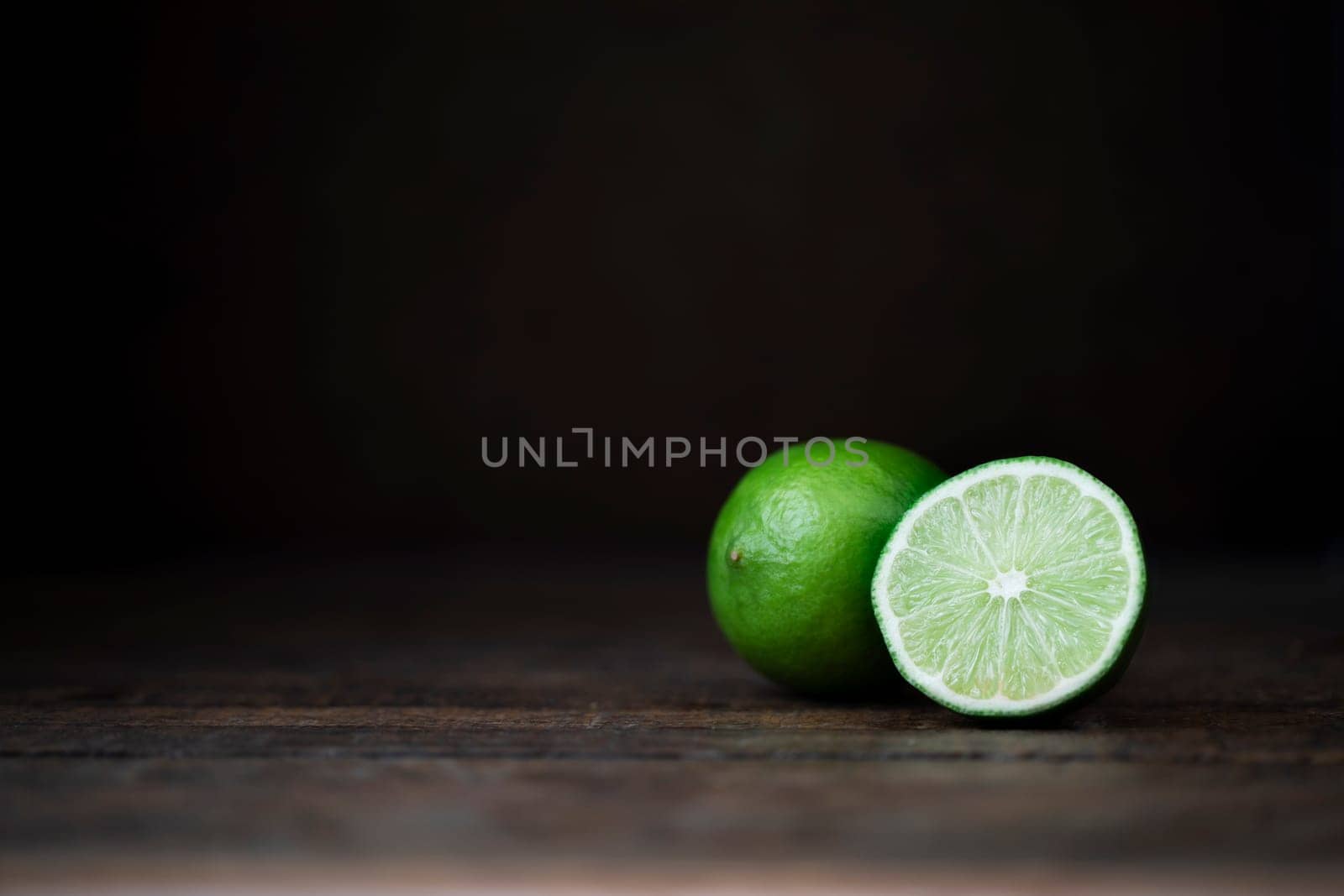 Whole and half lime on wooden surface with copy space.