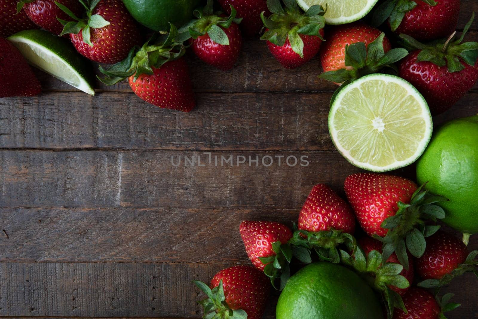 Flat lay of fresh lime and strawberries on dark wooden sufrace with copy space