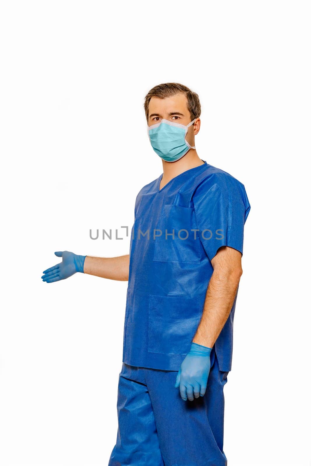 Male doctor in scrubs wearing protective face mask and gloves inviting patients for health check. Plain white background. Coronavirus concept