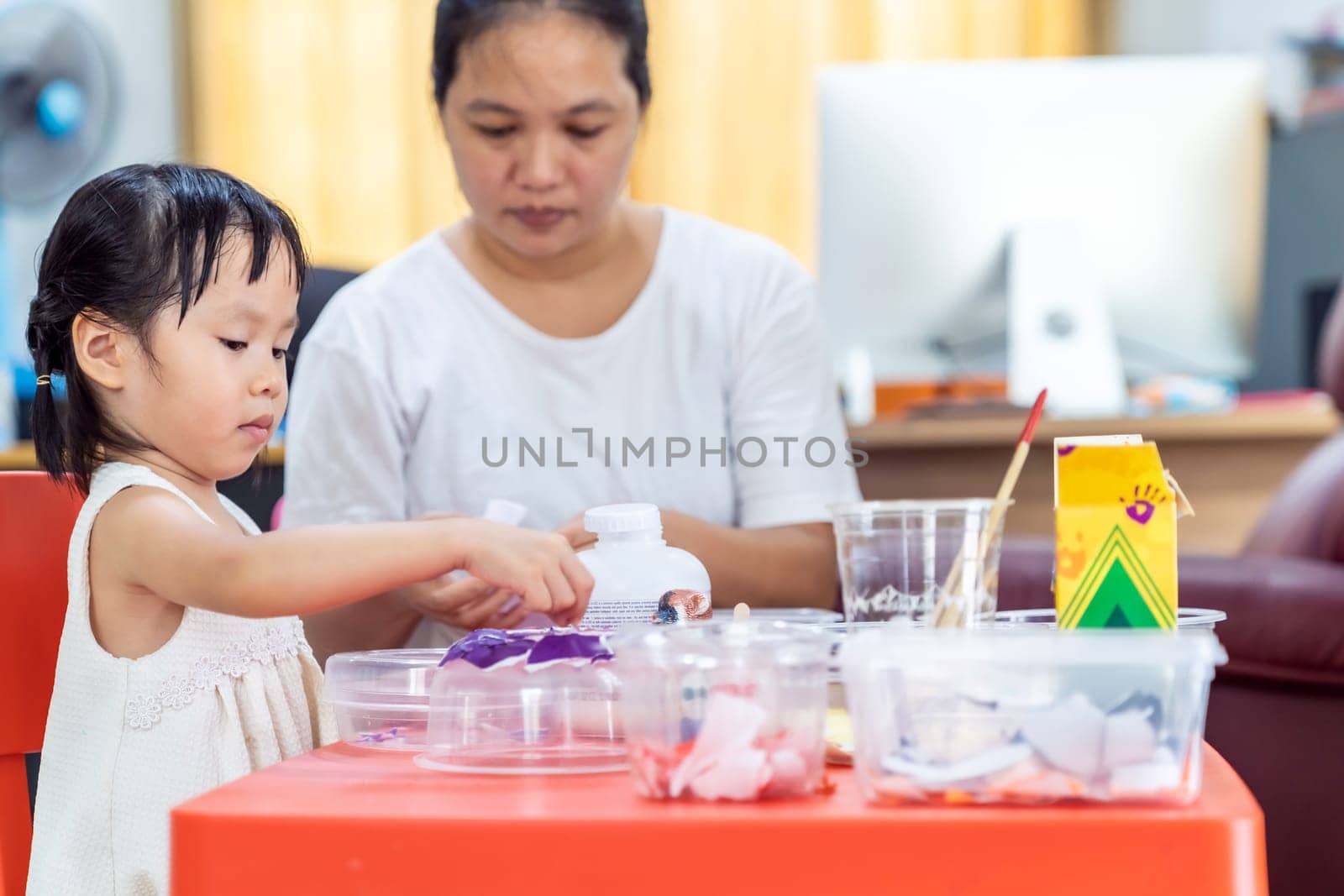Asian girl kid playing toy and colorful paper for art lesson at living room in home as home schooling while city lockdown because of covid-19 pandemic across the world with quaratine mom as teacher.